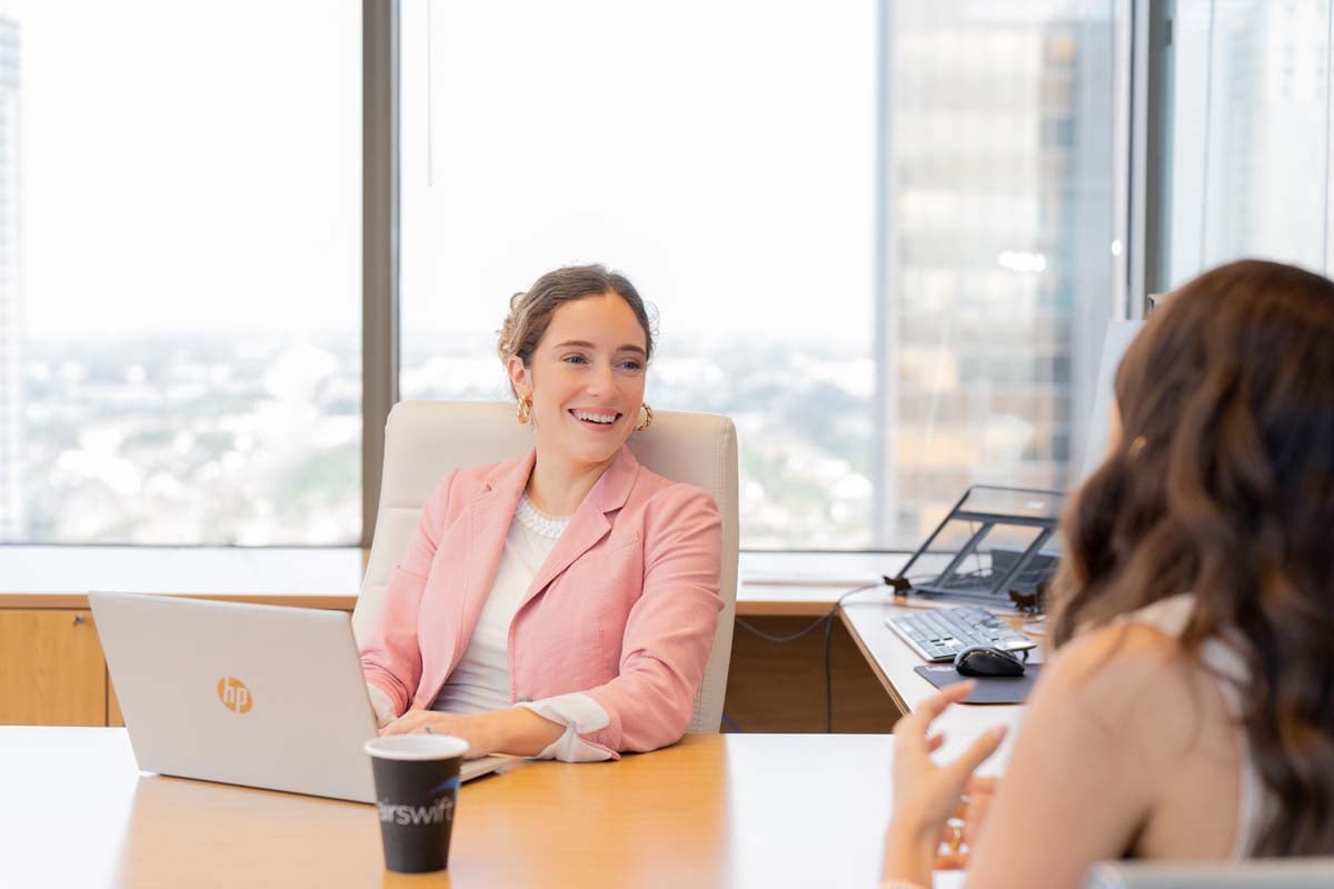 Woman smiling at her desk at a colleague with her laptop open